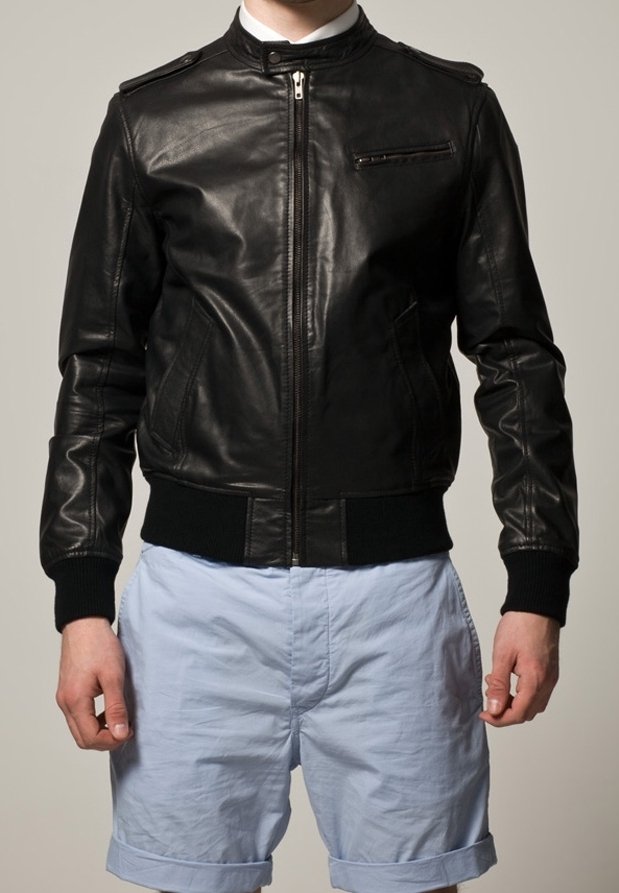 Svart läder bomberjacka med framdragkedja, sidofickor och bröstficka; ribbade cuffs och midja; slät textur. Ljusa shorts nedanför.