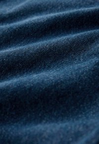 Tela de mezclilla en tono azul profundo, con una superficie texturizada que muestra el tejido visible y un ligero brillo, exhibiendo pliegues y arrugas.