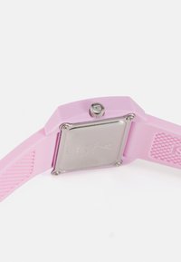 Montre en silicone rose avec un cadran carré en acier inoxydable. Équipée d'un bracelet texturé et d'une couronne en métal sur le côté pour régler l'heure.