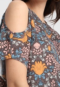 Hemd mit kalten Schultern aus dunkelbraunem Stoff, mit einem Blumenmuster in Orange, Blau und Pink und einer lockeren, entspannten Passform.