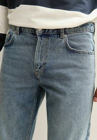 Jeans de mezclilla azul claro con un ajuste clásico, que presentan un diseño de cinco bolsillos, costuras en contraste y un acabado ligeramente desgastado.