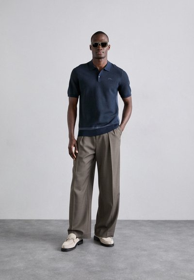 Polo marinero de manga corta con tejido texturizado, con una tapeta de dos botones. Combinado con pantalones de pinzas beige y mocasines de color claro.