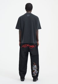 Černé oversized tričko s kulatým výstřihem, doplněné volnými černými džíny s červenou výšivkou "Ed Hardy" a barevným designem draka.