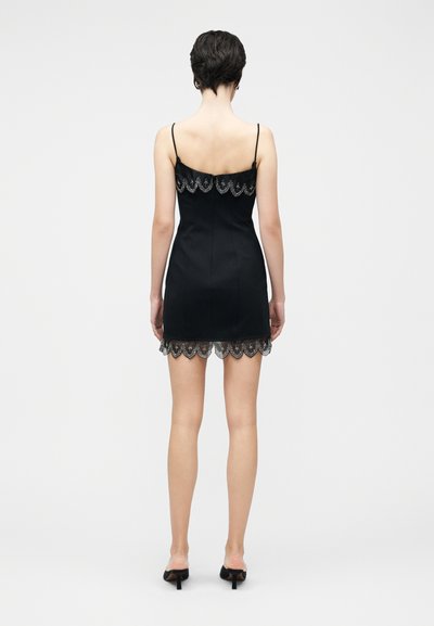 Melnā mini kleita ar regulējamām plānu lencītēm, ar viļņotu mežģīņu apmali un dekoratīvām izšuvēm aizmugurējā kakla izgriezumā.