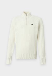 Kremna pletena zip-up jopica z rebrastim teksturo, visokim ovratnikom in majhnim zelenim logotipom na levem prsnem delu. Dolgi rokavi in prilagojen rob.