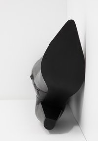 Botín negro de tacón alto con punta afilada y cuero texturizado. Acabado suave y un tacón afinado con una sutil suela negra.