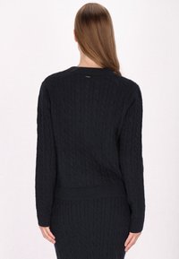 Maglione in maglia navale con maniche lunghe, polsini e orlo a coste, caratterizzato da un scollo rotondo e un discreto dettaglio con etichetta sul retro.