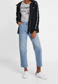 Černá lehká bunda s logem, šedé tričko s grafikou, světle modré zkrácené džíny s třepeným lemem a bílé tenisky.