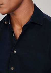 Marine corduroy overhemd met een puntige kraag, knoopsluiting en een gestructureerde stof. Bevat lichtgekleurde knopen en een subtiel geribbeld patroon.