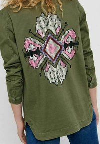 Camicia verde oliva con maniche lunghe, caratterizzata da un design ricamato colorato sulla schiena con dettagli in rosa, grigio e nero.