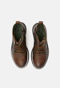 Botas de cuero marrón hasta el tobillo con suelas de goma oscuras, que presentan cordones verdes, un zipper lateral y un forro interior con un patrón.