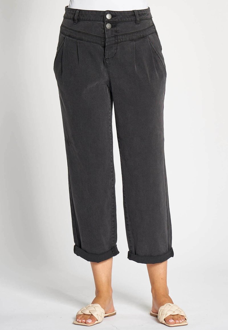 Schwarze, hoch taillierte, verkürzte Hosen mit umgeschlagenen Säumen, vorderen Falten, zwei seitlichen Taschen und zwei silbernen Knöpfen, getragen mit cremefarbenen Pantoletten.