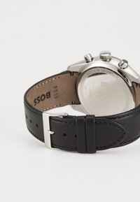 Bracelet de montre en cuir noir avec boucle en métal argenté, doté d'un boîtier en acier inoxydable et d'un dos en verre clair étiqueté "résistant à l'eau".