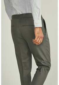 Šedé kalhoty na míru s hladkou texturou, dvěma zadními kapsami a úzkým střihem, doplněné modro-bílým pruhovaným tričkem.