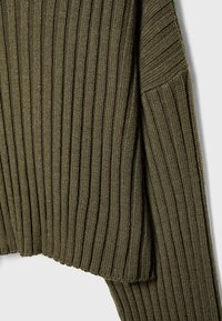 Olivengroene geribbelde trui van geweven stof. Het heeft lange mouwen en een aansluitende zoom, waarmee de verticale breipatronen worden benadrukt.