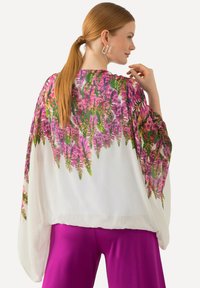 Květinové kimono s fialovými a zelenými vzory, průhledná bílá látka, široké rukávy, spárováno s živými růžovými kalhotami.