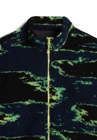 Fleece jack met een hoge kraag; bevat een abstract patroon in blauw, zwart en groen; ritssluiting met gele accenten.