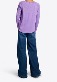 Lila Langarmshirt mit abgerundetem Saum und Raglanärmeln, kombiniert mit weit geschnittenen, dunkelblauen Jeans mit Gesäßtaschen.