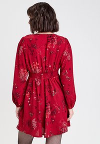 Red floral dress with long sleeves, smocked waist, and butterfly patterns. Made from lightweight fabric, featuring a slightly flared skirt.