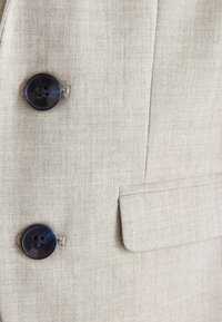 Ljusbeige blazers med strukturerad väv, två stora mörka knappar och en sidoficka. Enkel, klassisk design med en skräddarsydd passform.