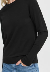 Maglione nero a maglia con maniche lunghe, polsini e orlo a costine, morbido al tatto, vestibilità rilassata, abbinato a jeans blu strappati.