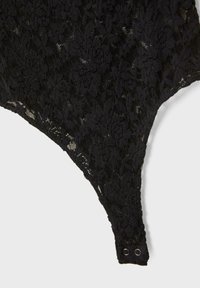 Body in pizzo nero con motivo floreale, tessuto testurizzato e chiusure a pressione nella parte inferiori. Design angolare con sezioni trasparenti.