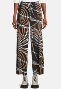 Breda byxor med svarta, bruna och grå abstrakta virvlar och randiga mönster, bärs med vita snörskor och en vit topp.