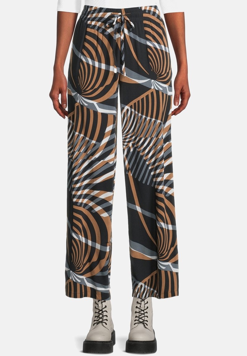 Breda byxor med svarta, bruna och grå abstrakta virvlar och randiga mönster, bärs med vita snörskor och en vit topp.