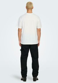 T-shirt bianco a maniche corte, vestibilità classica, abbinato a pantaloni cargo neri con tasche laterali e un design gamba leggermente affusolata.