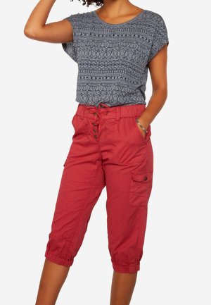 Granatowy top z krótkim rękawem o teksturowanych geometrycznych wzorach oraz czerwone spodenki o kroju na wysokości kostek z elastycznym paskiem, zapięciem na guziki i kieszeniami bocznymi.