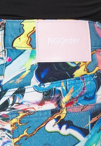 Barevné džíny z denimu s abstraktními vzory. Vybaveny růžovým štítkem s nápisem "NGOrder" vytištěným bílou barvou. Detailní pohled na švy a texturu.