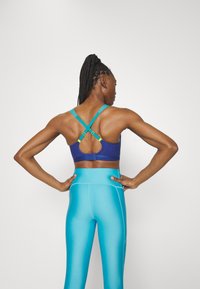 Sujetador deportivo azul con tirantes cruzados y acentos amarillos, combinado con leggings de talle alto en un brillante tono turquesa que presentan una textura suave.
