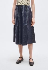 Fustă midi bleumarin cu o textură lucioasă și creponată. Dispune de o talie elastică și o siluetă relaxată, în formă de A. Poartă pantofi comozi în nuanțe închise.