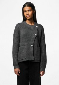 Tamsiai pilkas, briaunotas mezginys kardiganas su apvalia iškirpte, sagų uždarymu, dviem priekinėmis kišenėmis ir tekstūruotais rankovėmis.