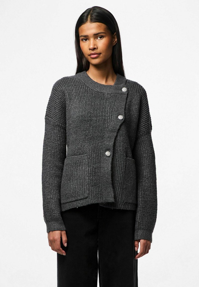 Tamsiai pilkas, briaunotas mezginys kardiganas su apvalia iškirpte, sagų uždarymu, dviem priekinėmis kišenėmis ir tekstūruotais rankovėmis.