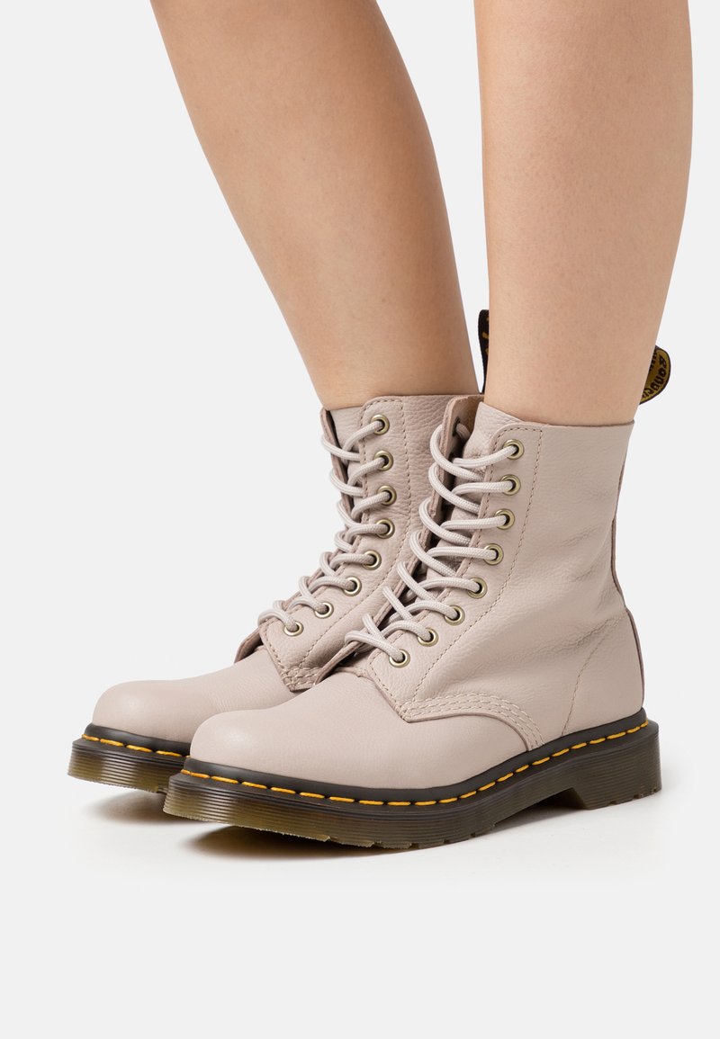 Botas de tobillo de cuero color rosa claro con punta redondeada, diseño de cordones y costuras amarillas a lo largo de la suela. Presenta un acabado texturizado.