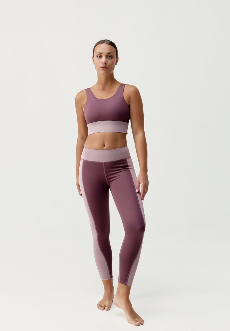 Zestaw biustonosza sportowego i legginsów w głębokim mauve z jaśniejszymi akcentami mauve. Miękki, elastyczny materiał, dopasowany krój, minimalne detale szwów.