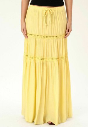 Żółta, wielowarstwowa spódnica maxi z koronkową lamówką i ściągaczem w pasie, noszona z czarnym topem i sandałami, widok z przodu od talii w dół.