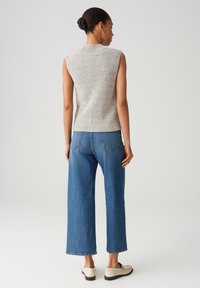 Light gray sleeveless knit top with a textured finish, paired with high-waisted blue wide-leg jeans and beige shoes.