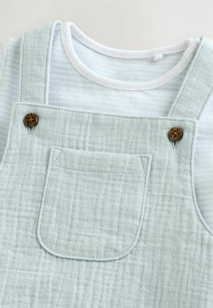 Light blue, textured overalls feature wooden buttons and a front pocket, paired with a white and blue striped shirt beneath.