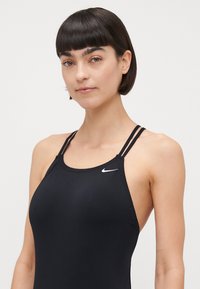 Zwarte zwempak met een strak ontwerp, gemaakt van glad materiaal. Voorzien van dunne banden en een klein wit Nike-logo op de borst.