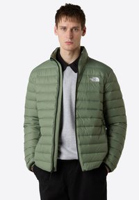 Giacca a vento verde con design trapuntato, colletto alto e zip frontale. Presenta un logo sul petto e due tasche laterali con zip.