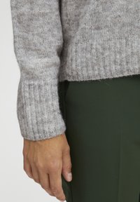 Grå ribstrikket sweater med blød tekstur, der har tætsiddende manchetter og en let løs pasform, parret med mørkegrønne bukser.