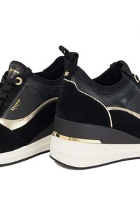 Black suede trainers with gold accents and a textured panel. Features a wedge sole and lace-up design with a pull tab at the heel.
