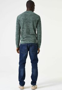 Groen gemêleerd trui met lange mouwen, gecombineerd met donkerblauwe spijkerbroek. De trui heeft een ronde hals en golven van kleurvariatie.