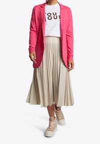 Rosa blazer över en vit t-shirt med brun text, tillsammans med en plisserad beige midikjol och beiga högtoppssneakers.