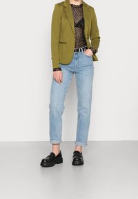 Zelený blazer, černý top s puntíky ze síťoviny, světle modré džíny a masivní černé mokasíny. Blazer má jedno knoflík a klopové límce.
