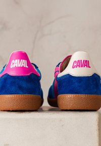 Paire de baskets en daim bleu avec semelles marron, languettes de talon roses et blanches, chacune marquée d'un grand texte "CAVAL" rose ou blanc.