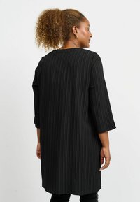 Schwarzes gestreiftes Tunika-Kleid mit drei Viertelärmeln, geradem Schnitt und softem Material. Der Stoff hat ein dezentes Rippmuster.