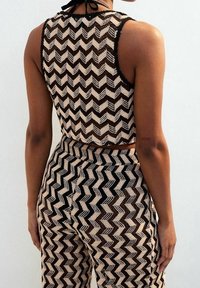 Pletený dvoudílný outfit v béžové a černé zigzagové vzoru. Top je zkrácený s vysokým výstřihem a zavazováním na zádech; kalhoty jsou těsně přiléhavé s vysokým pasem.